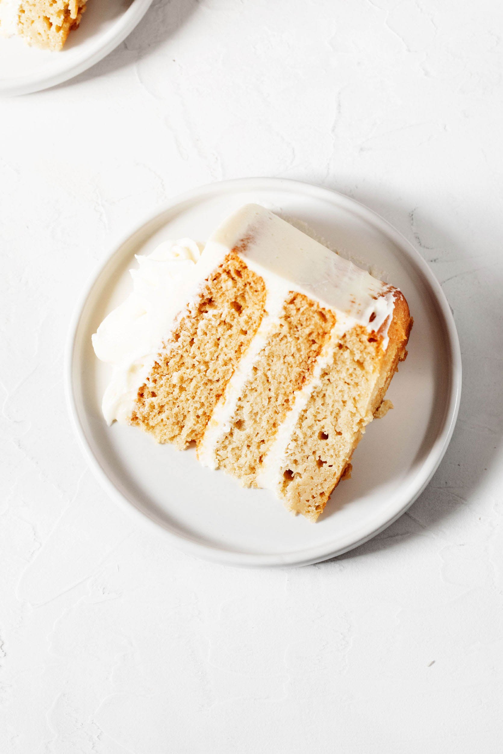 An overhead image of a slice of vegan vanilla cake, which has been sliced and placed onto a round dessert plate.
