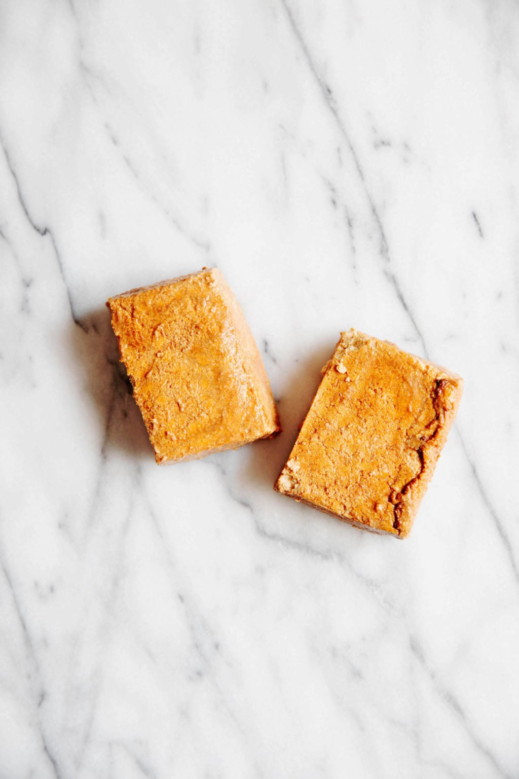 Two blocks of marinated, baked tofu rest on a marble surface.