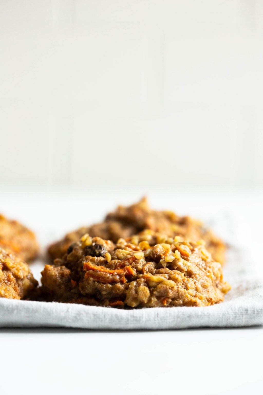 A few chewy, oatmeal breakfast cookies are placed on a pale linen napkin against a bright backdrop.