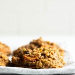 A few chewy, oatmeal breakfast cookies are placed on a pale linen napkin against a bright backdrop.