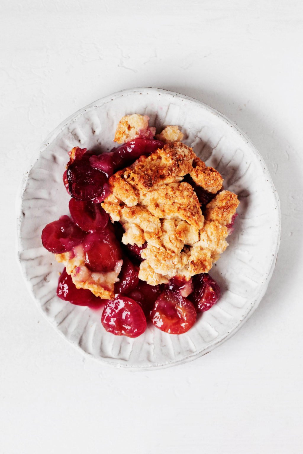 A small, fluted white plate is topped with a serving of vegan cherry pie, made with a crumbly biscuit crust.