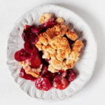 A small, fluted white plate is topped with a serving of vegan cherry pie, made with a crumbly biscuit crust.