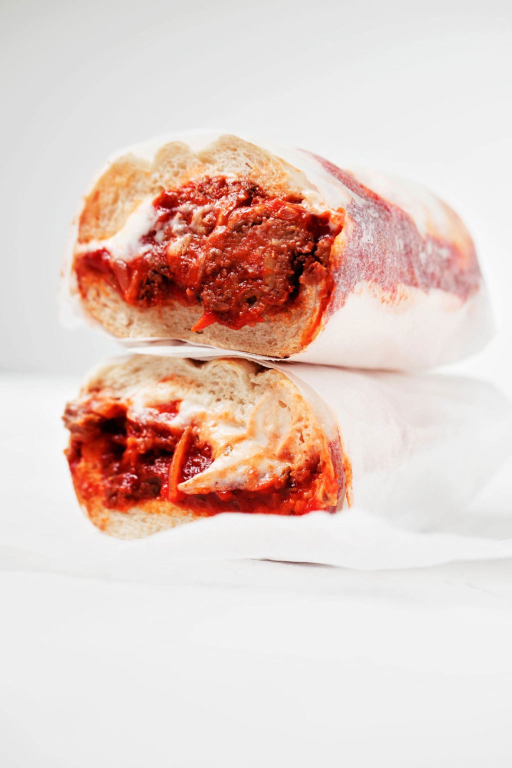 A vegan tempeh meatball sub is wrapped in parchment paper and resting on a white surface. 