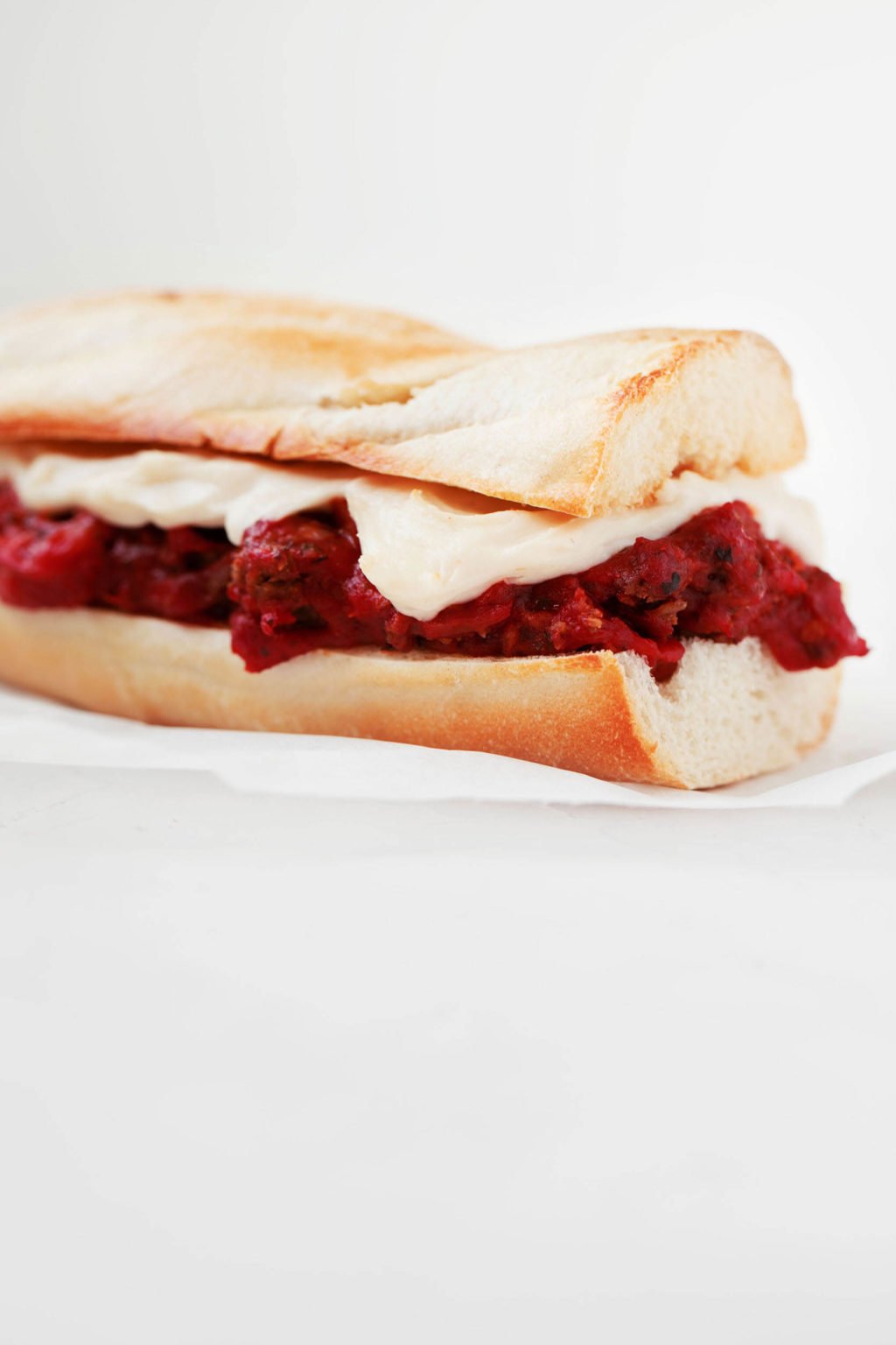 An angled photograph of a vegan tempeh meatball sub, which is resting on white parchment.