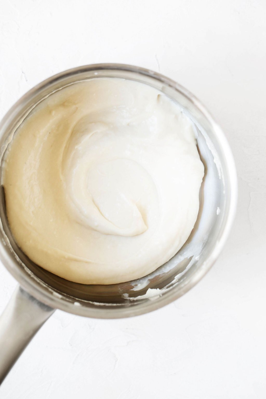 An overhead image of a creamy, white sauce, which is held in a small metal saucepan.