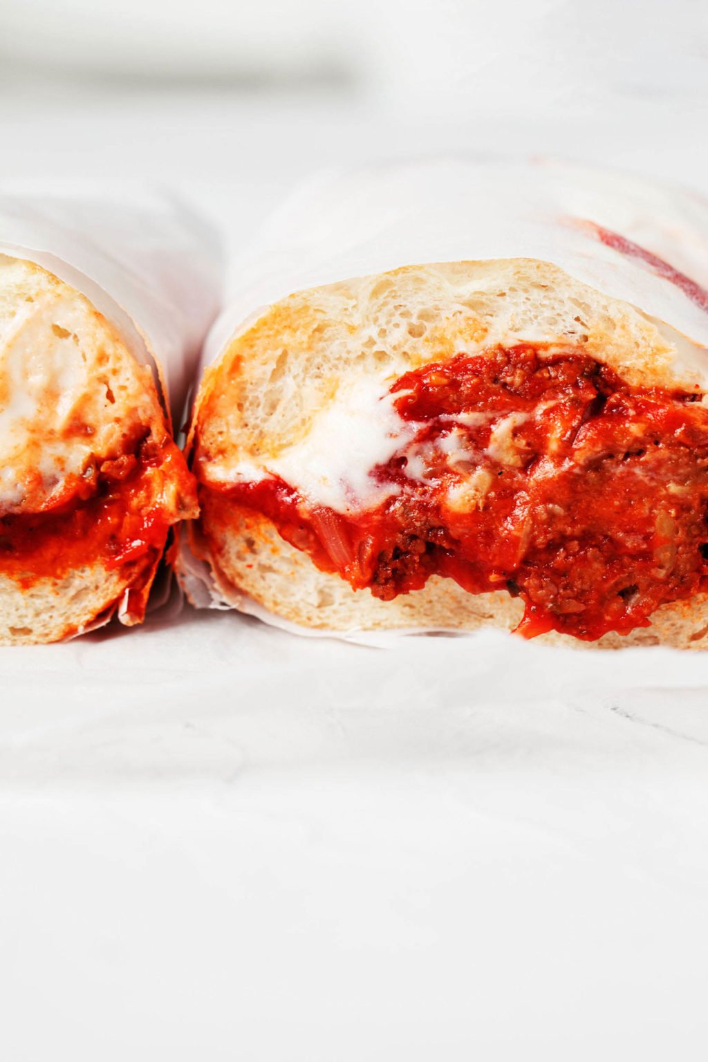 A vegan Italian meatball sub, made with tempeh, has been sliced in half crosswise. A cross section of the sandwich is shown against a white background.