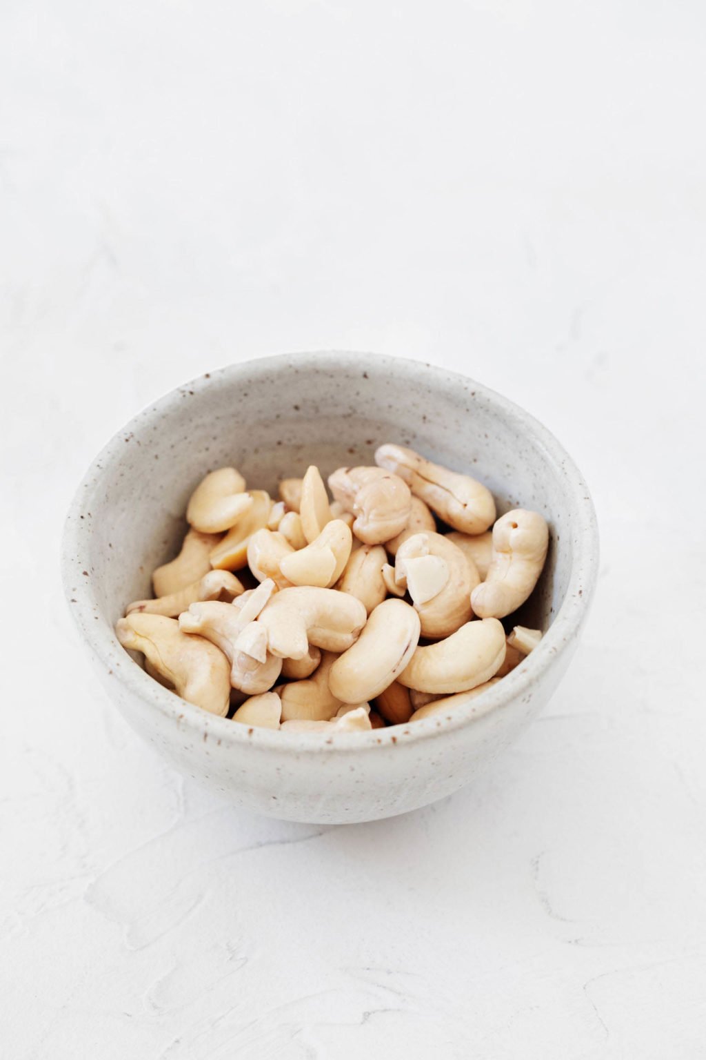 A small, ceramic pinch bowl is filled with nuts. It rests on a white surface.
