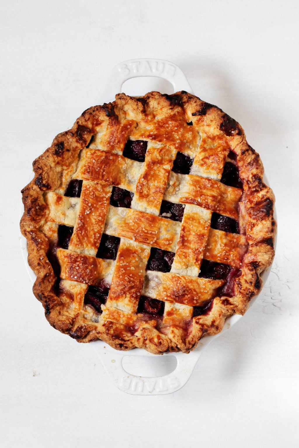 A dark golden, freshly baked fruit dessert with a lattice top crust is resting in a white round baking dish.