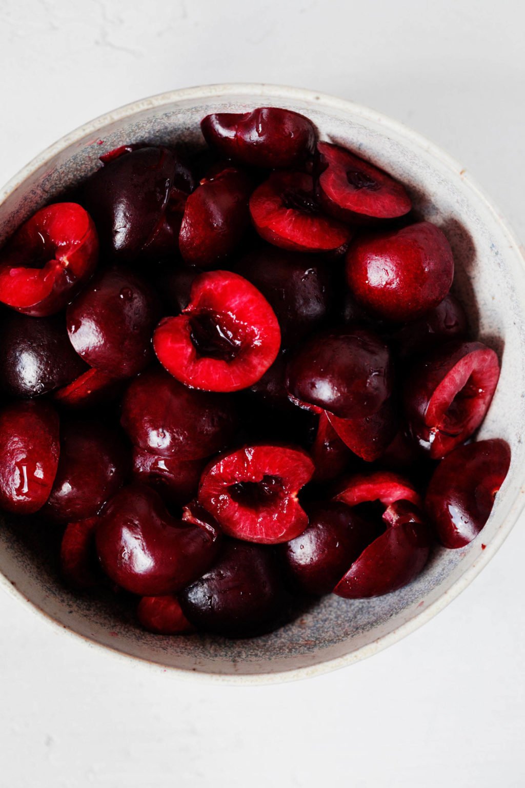 A small bowl is filled with halved, dark sweet cherries.