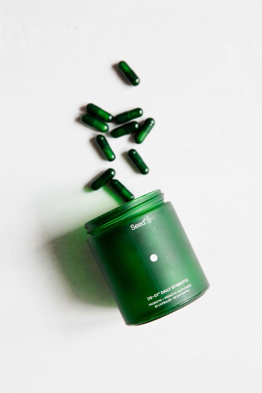 A green bottle is laid on a white surface, with green capsule shaped pills tumbling out beside it.