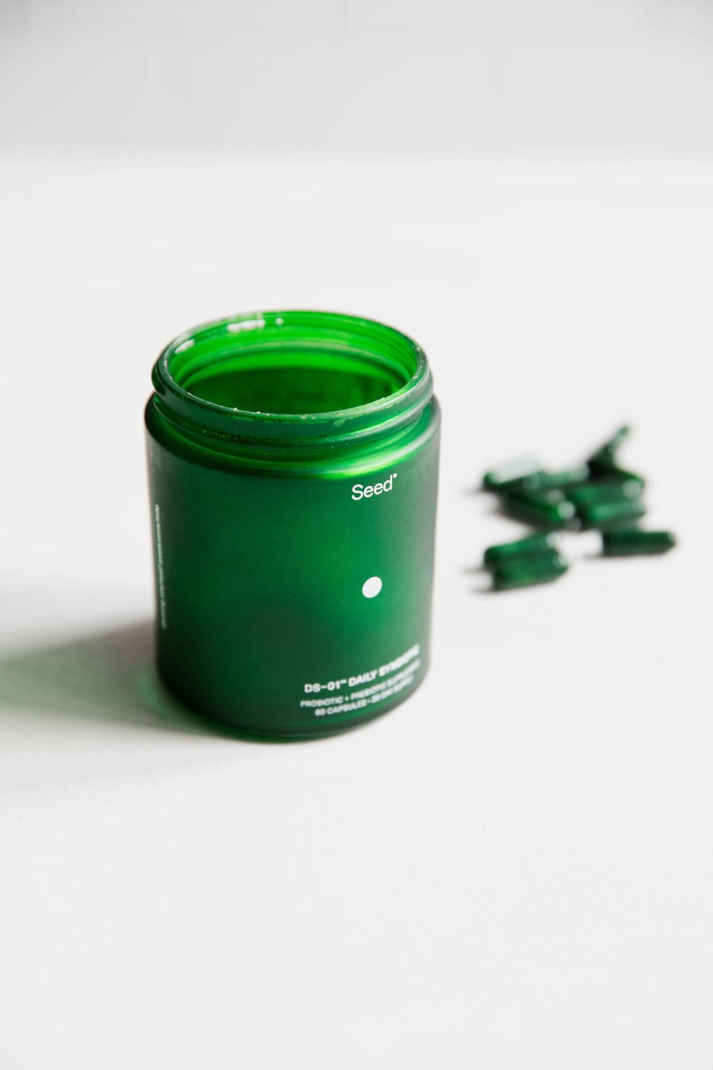 A green, glass pill bottle is standing atop a white surface.