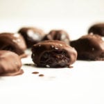 Medjool dates that have been drizzled with dark chocolate and sea salt are arranged on a white surface.