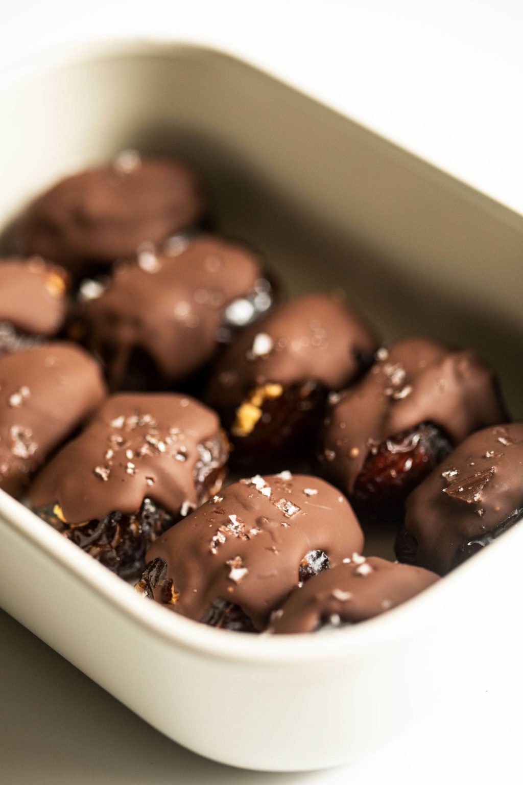 A white storage container holds chocolate dipped vegan treats.