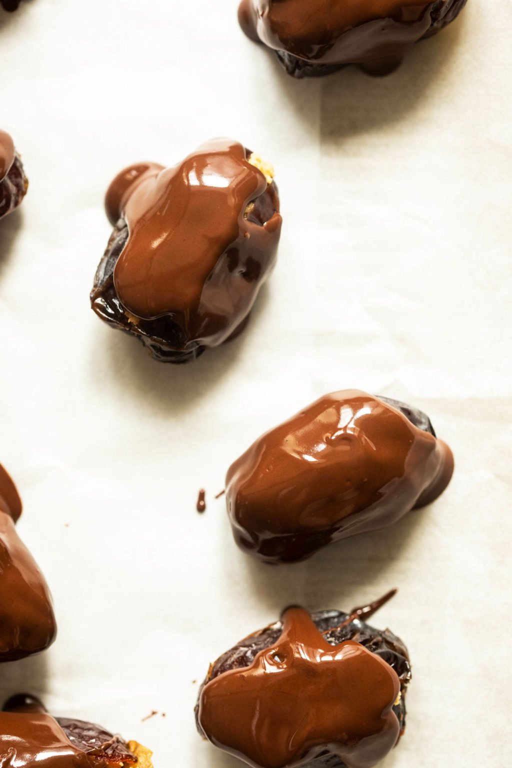 Medjool dates have been drizzled with dark chocolate on a parchment lined baking sheet.