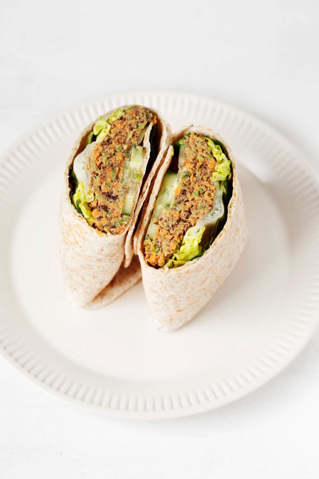 A vegan lentil tahini wrap has been sliced in half. It's placed, cut side up, on a cream colored serving dish.