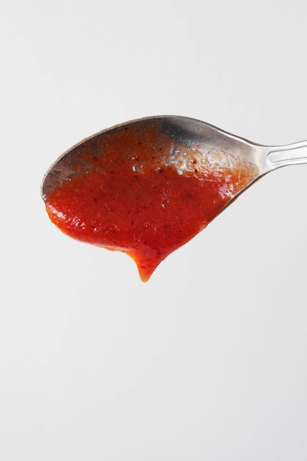 A metal spoon has been coated with a thick, red-orange sauce.
