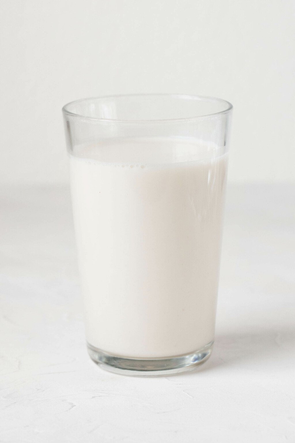 A tall, clear glass holds almond milk. It's resting on a white surface.