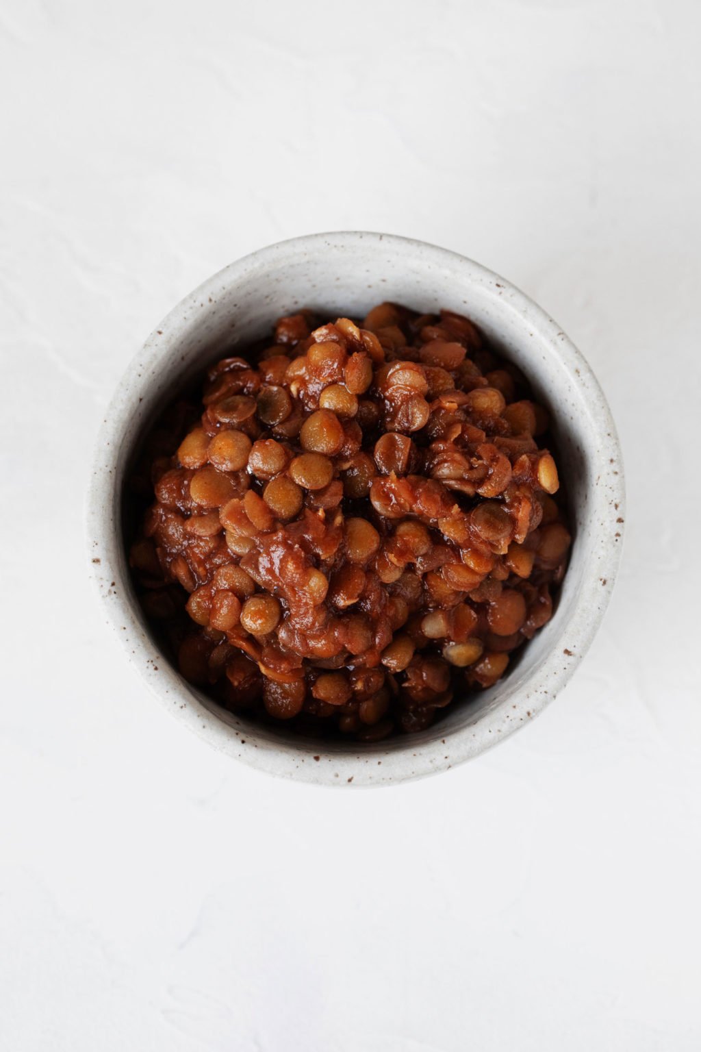 A small, white bowl is filled with reddish brown, BBQ lentils.