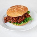 A sesame seed burger bun has been piled with BBQ lentils and a curly piece of bright green lettuce.