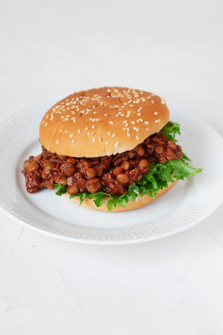 A sesame seed burger bun has been piled with BBQ lentils and a curly piece of bright green lettuce.