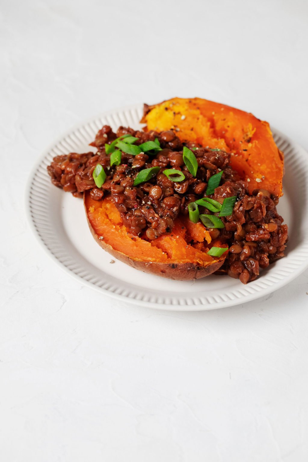 A baked yam has been split open and topped with a vegan protein, along with a sprinkle of chopped green onion tops.