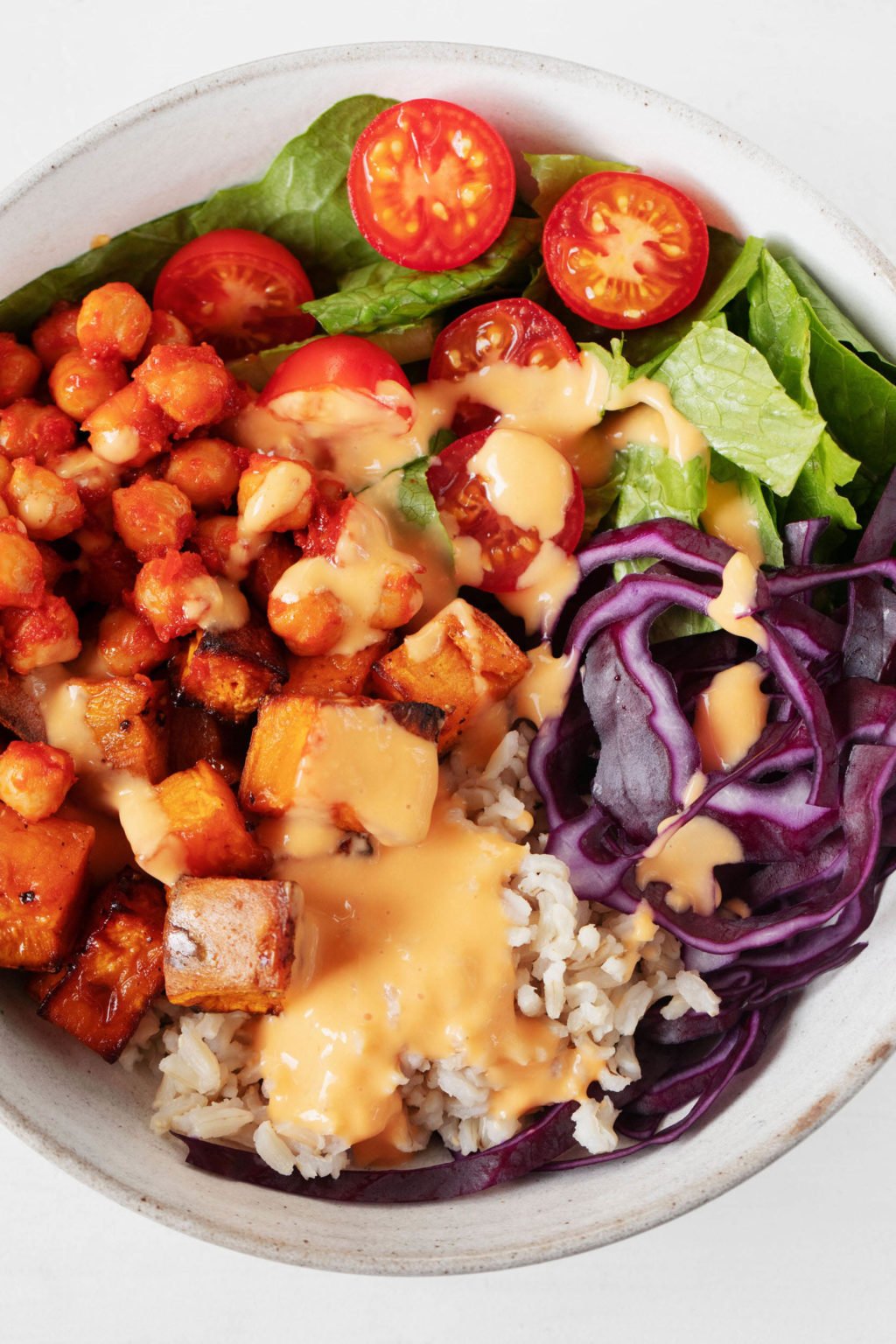 A close up, overhead image of a vibrant and colorful vegan chickpea burrito bowl. It's topped with a creamy cashew-based sauce.