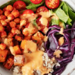 A close up, overhead image of a vibrant and colorful vegan chickpea burrito bowl. It's topped with a creamy cashew-based sauce.