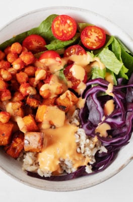 A close up, overhead image of a vibrant and colorful vegan chickpea burrito bowl. It's topped with a creamy cashew-based sauce.