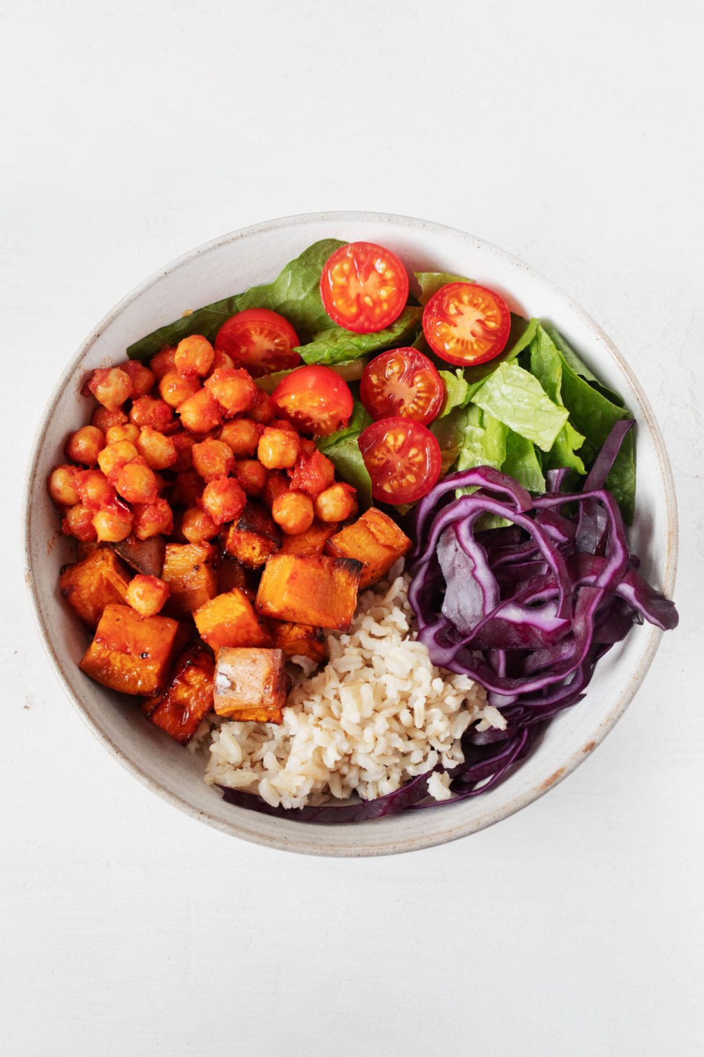 An overhead image of a white bowl containing seasoned chickpeas, rice, and vegetables.