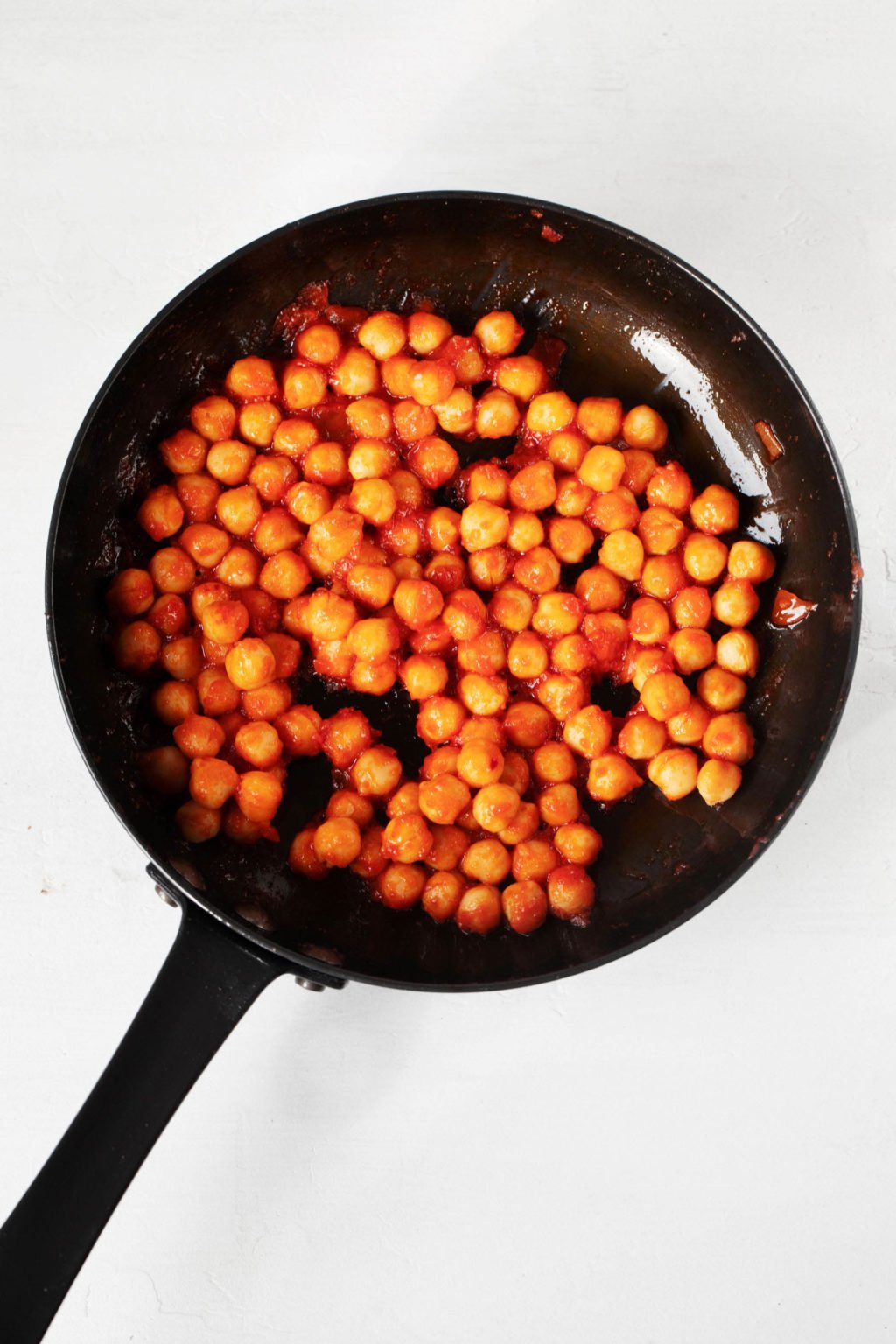 A small, black frying pan has been filled with beans that are tossed in a tomato based sauce.