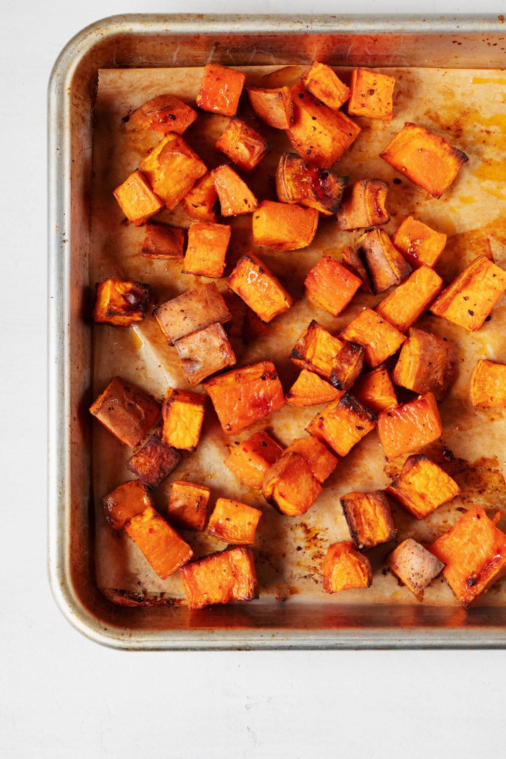 A lined sheet pan has been covered with cubes of roasted sweet potato. 