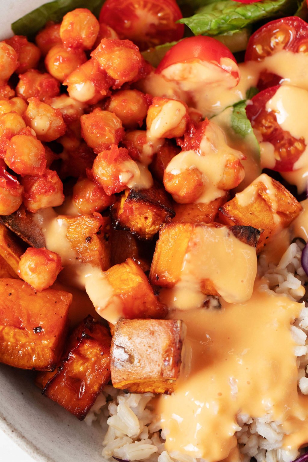 A zoomed in, overhead image of roasted sweet potatoes and chickpeas that have been smothered in a creamy, light orange colored sauce. 