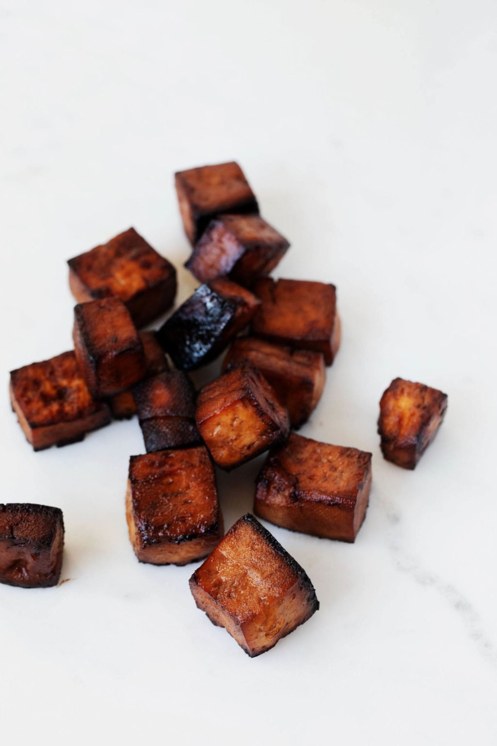 Tofu cubes, which have been marinated and baked, are lying in a small pile on a white surface. 