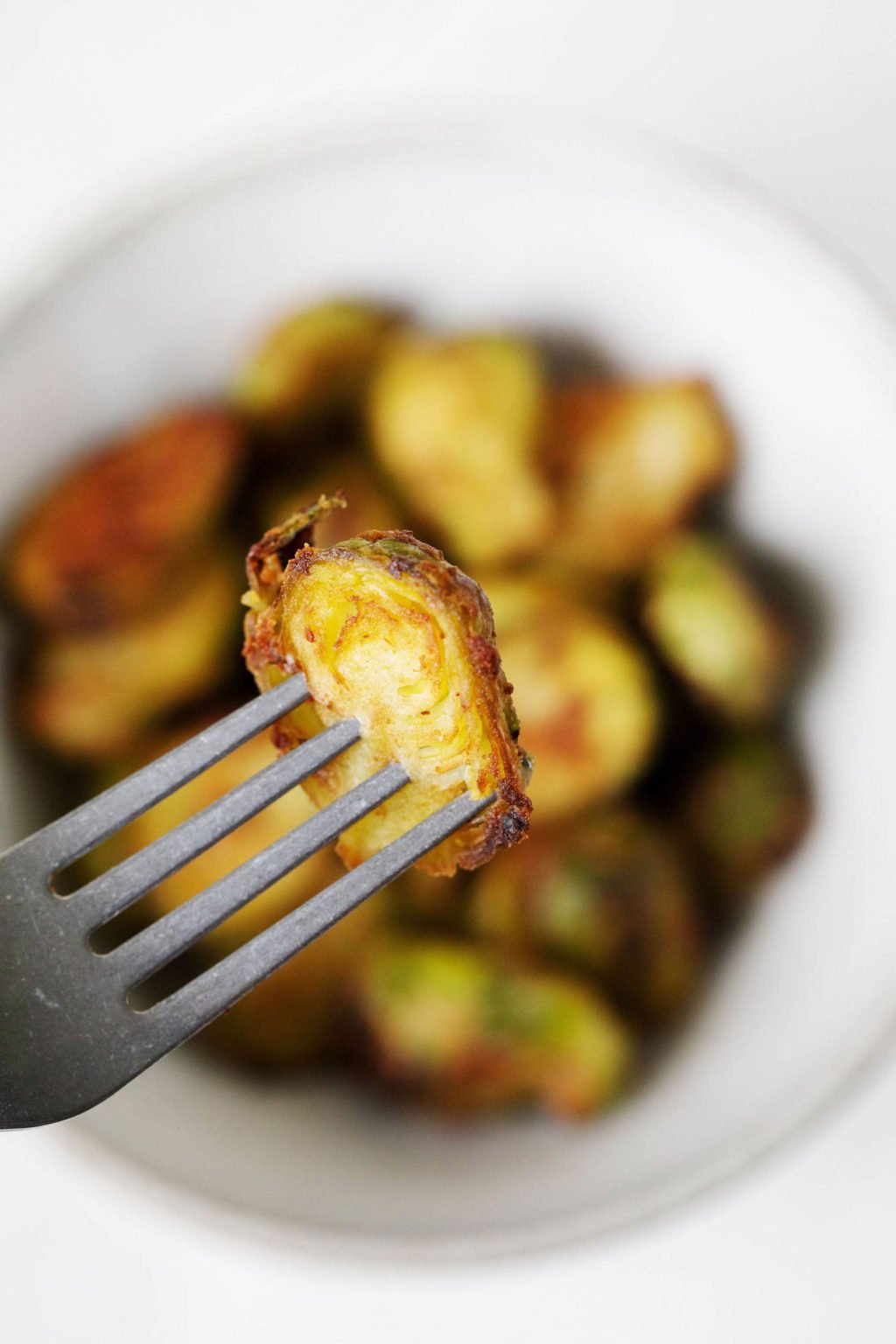 A silver fork pierces a single miso butter roasted Brussels sprout. Other sprouts peek out in the background.