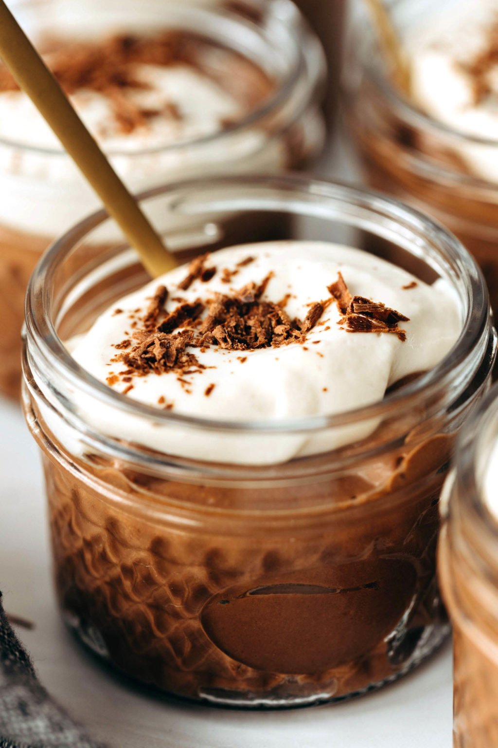 A few small mason jars are filled with chocolate pudding and tofu whipped cream. A spoon peeks out from one of them.