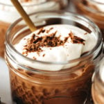 A few small mason jars are filled with chocolate pudding and tofu whipped cream. A spoon peeks out from one of them.