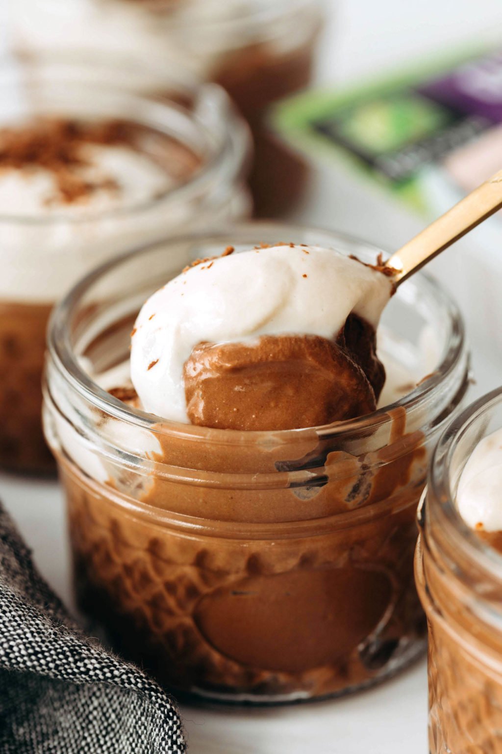 A mixture of chocolate pudding and tofu whipped cream is held in a small glass jar. It's being scooped out with a gold spoon.