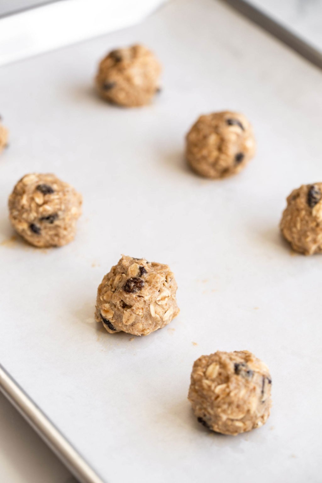 Cookie dough is resting in round balls on a lined baking sheet.
