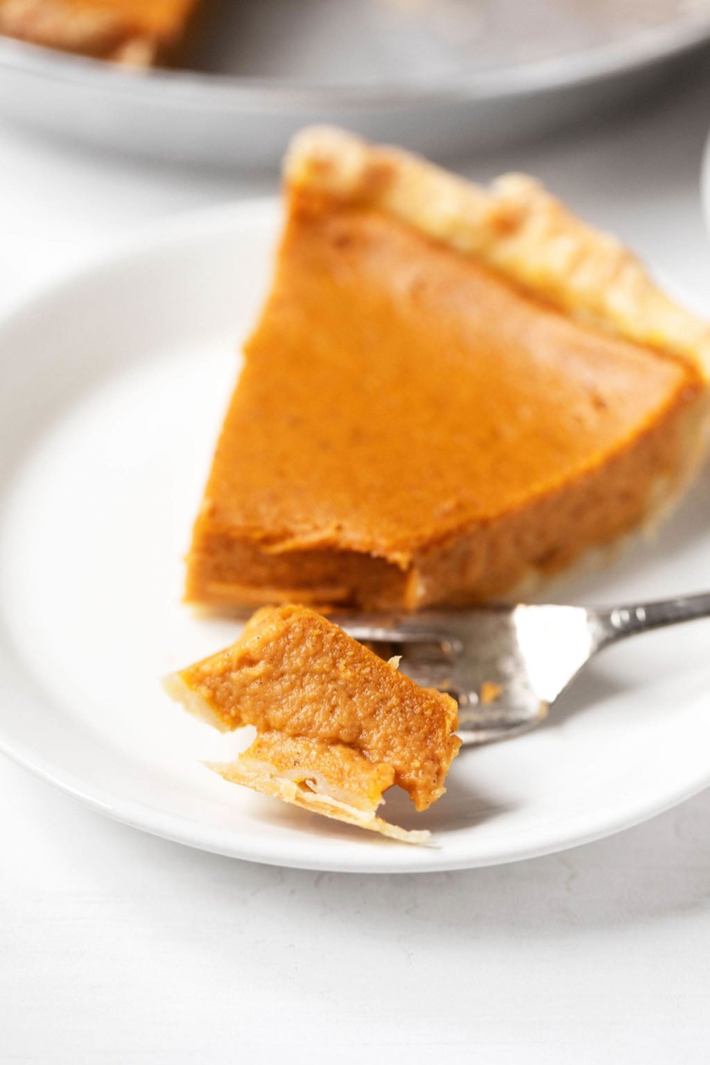 A single slice of vegan pumpkin pie has been cut into with a metal fork. It has a firm, light orange interior.