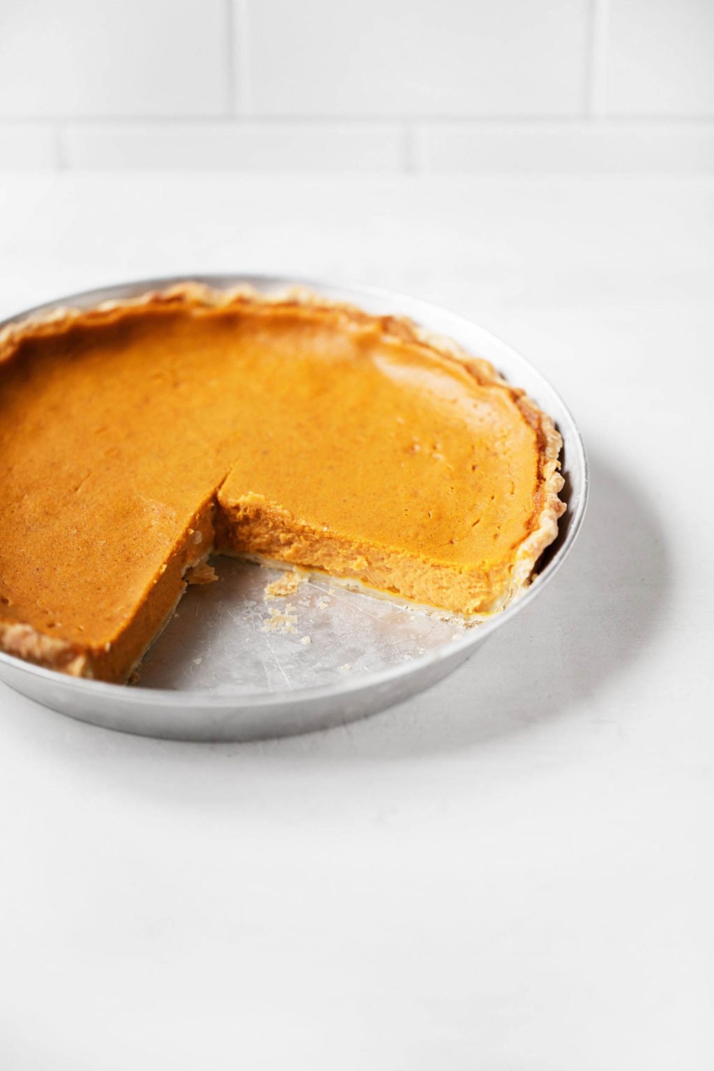 A round pie is served in a silver pie tin. A large slice has been cut out.