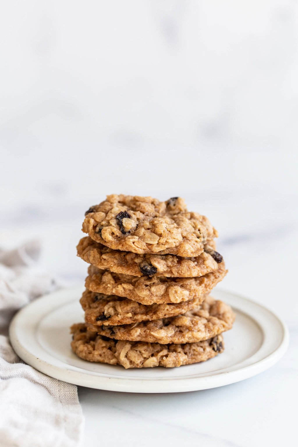 A stack of chewy vegan oatmeal raisin cookies rests on a small white plate.