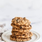 A stack of chewy vegan oatmeal raisin cookies rests on a small white plate.