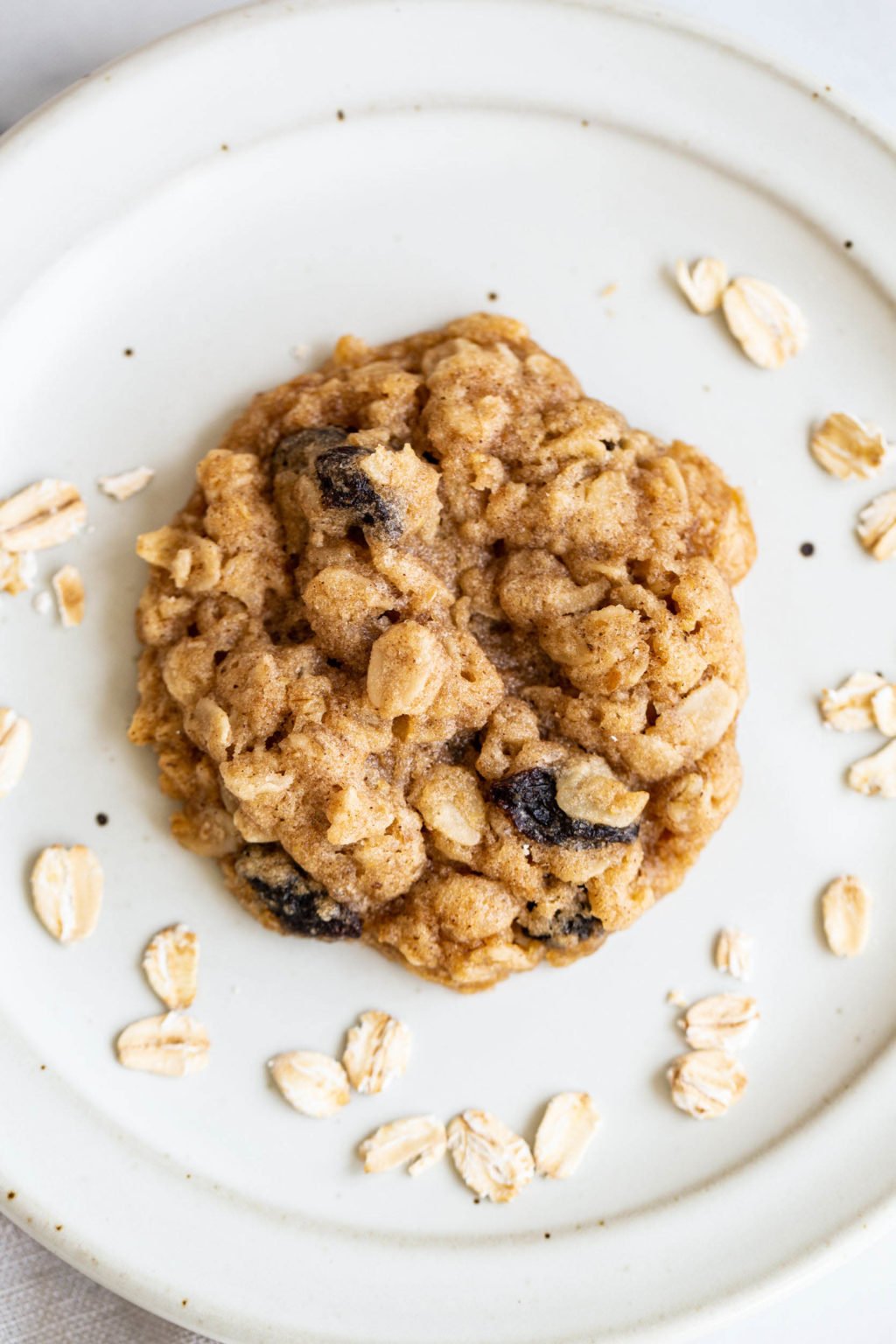 A single, chewy oatmeal raisin cookie rests on a white plate.