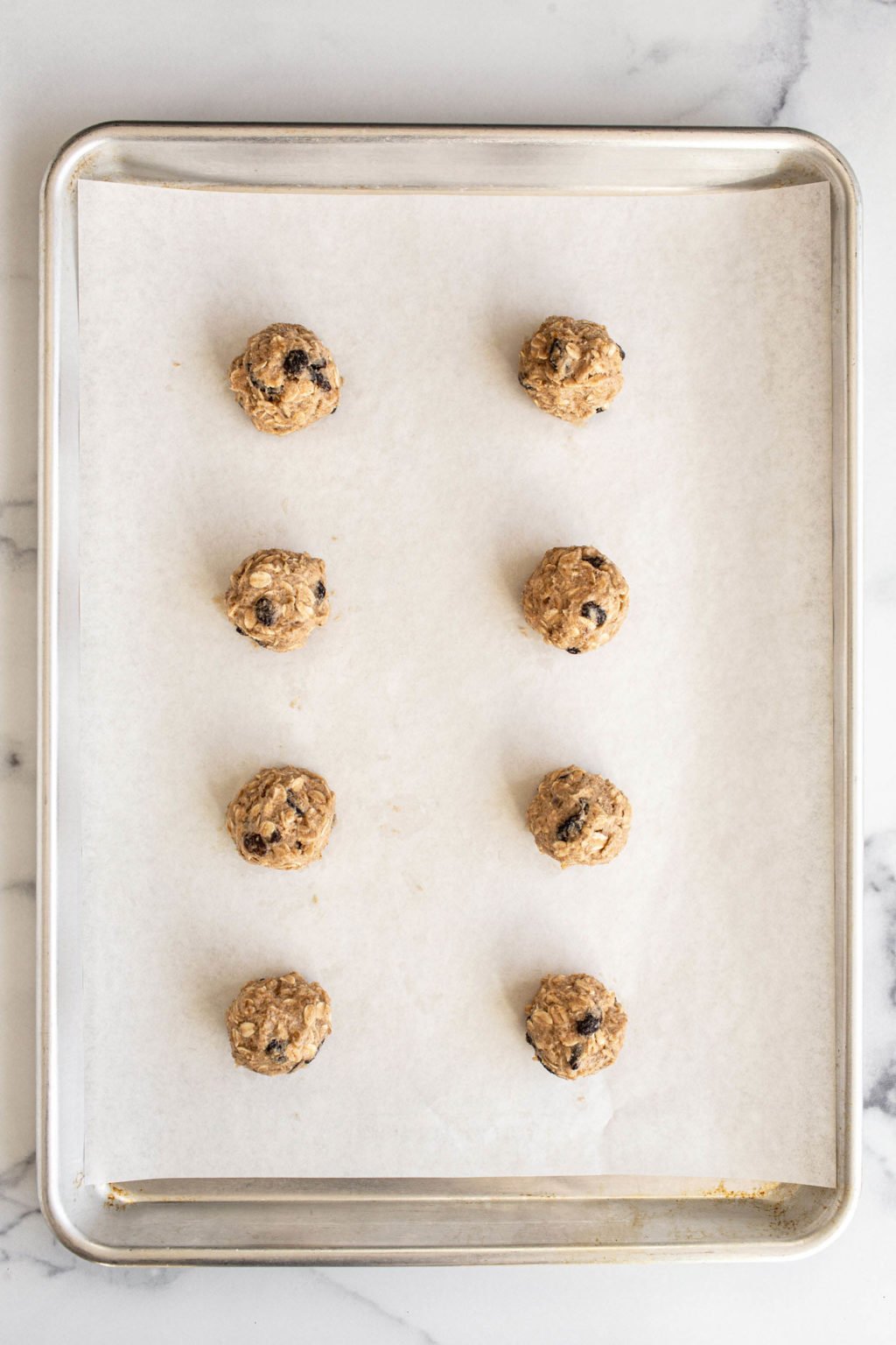Neat, round balls of cookie dough rest on a lined baking sheet.