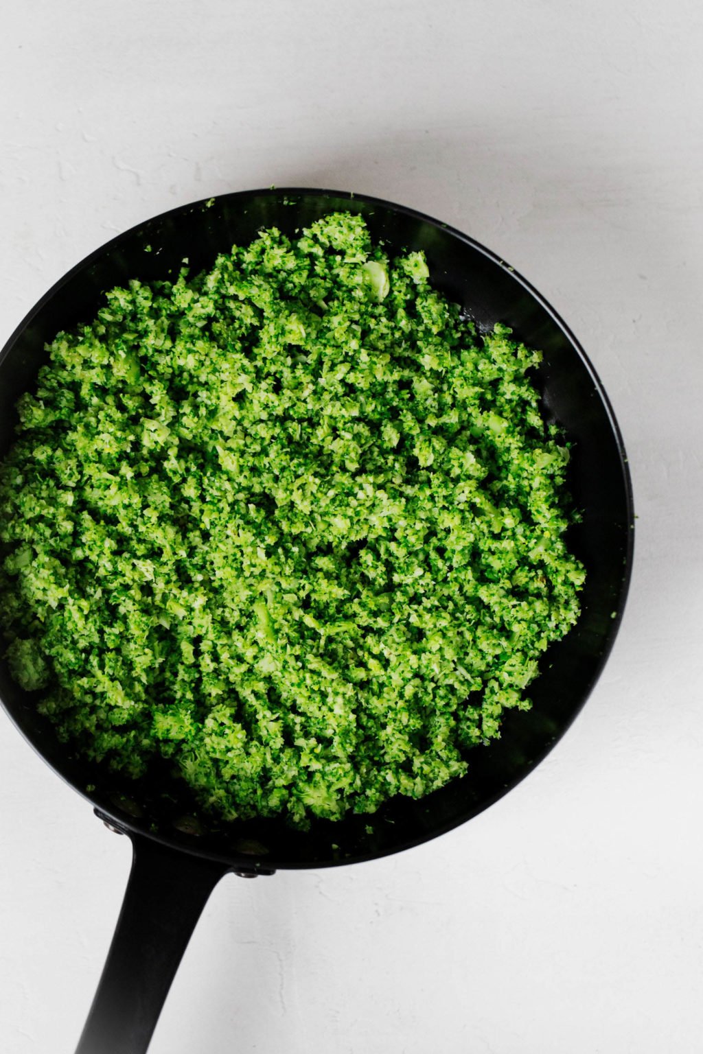 A black, cast iron skillet is full of finely chopped, lightly steamed broccoli.