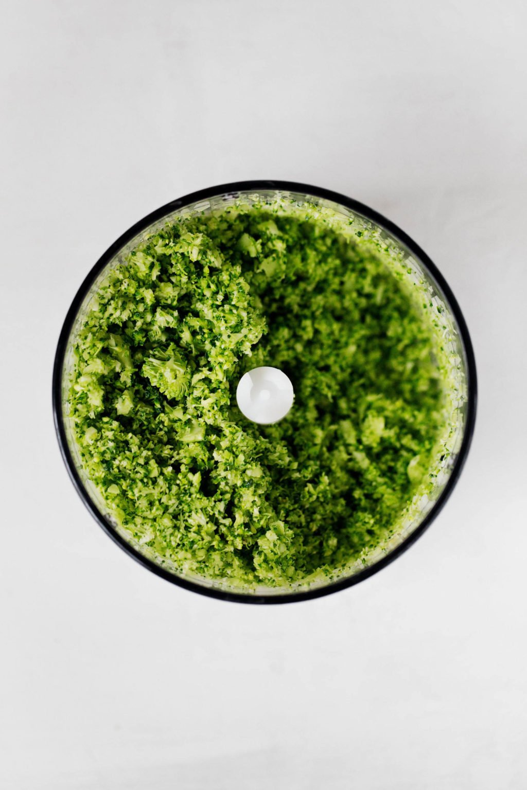 The bowl of a food processor is filled with chopped, lightly steamed green vegetables.