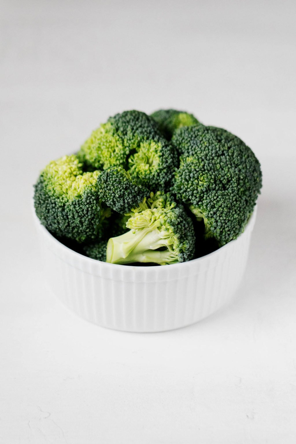 A small white ramekin is filled with raw broccoli florets.