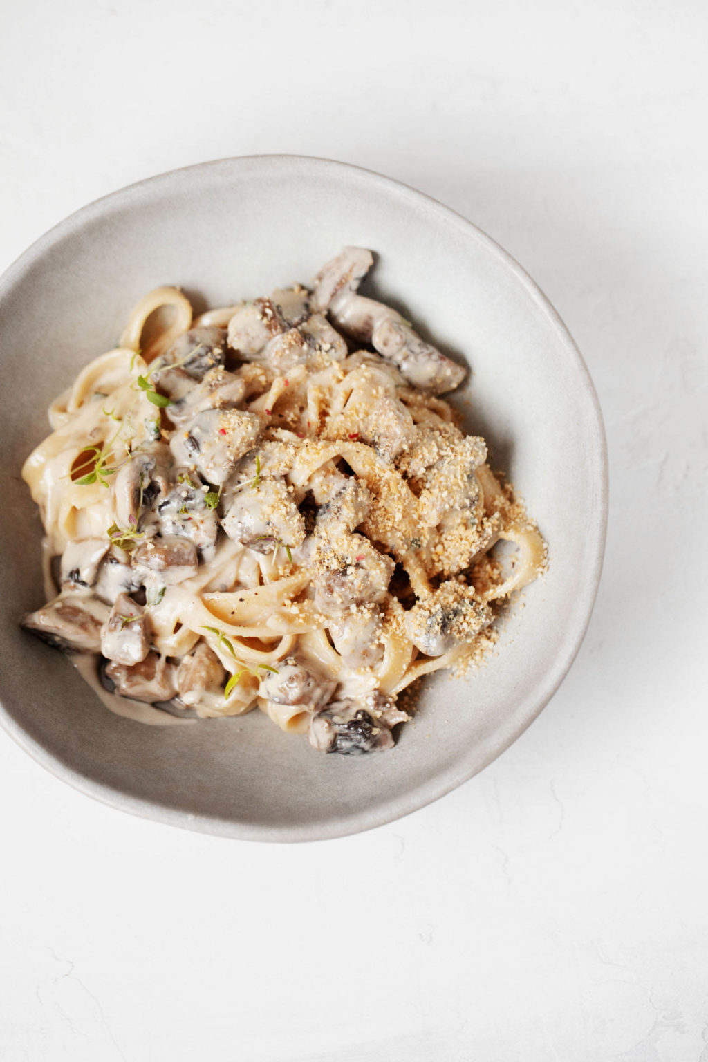 An overhead image of a bowl of creamy vegan mushroom pasta. It's topped with cashew parmesan cheese.