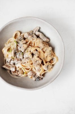 An overhead image of a bowl of creamy vegan mushroom pasta. It's topped with cashew parmesan cheese.