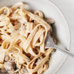 A creamy vegan mushroom pasta is being twirled on a fork. It rests in a round bowl.